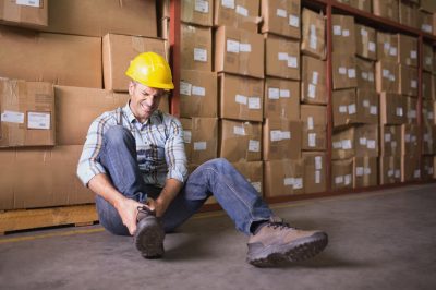 Male worker sitting with sprained ankle on the floor in warehouse